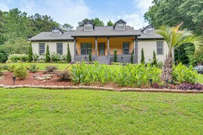 A two-story house with a front porch, a well-maintained lawn, and a variety of plants and shrubs.