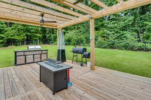 A wooden deck with a grill, a barbecue, and a table with drawers.