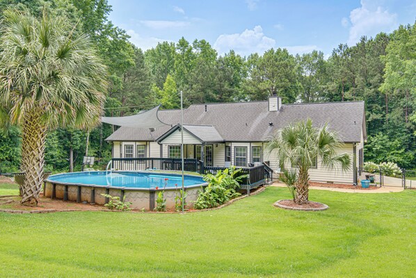 A two-story house with a swimming pool, surrounded by a well-maintained lawn and trees.