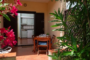 Eine Terrasse mit Tisch und Stühlen, eine durchgehende Tür zur Küche und ein Blumentopf.