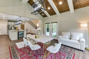 A spacious living area with a white sofa, a dining table with chairs, a kitchen in the background, and a staircase leading to another level. - On Several Acres! Luxury Home in Prairieville (Prairieville)