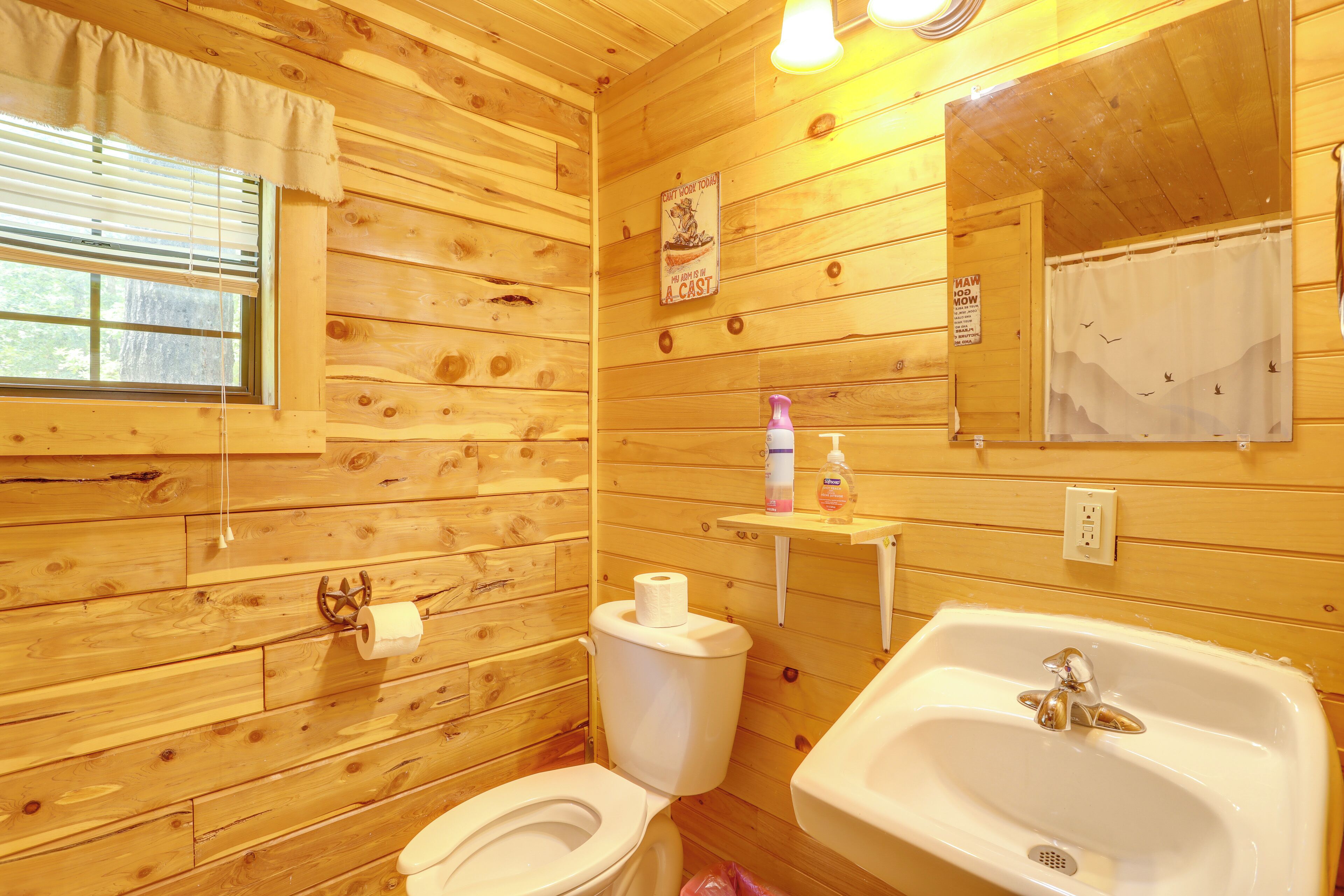 A wooden cabin bathroom with a toilet, sink, and mirror.