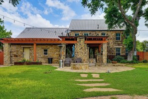 A stone building with a patio area, outdoor seating, and a stone fireplace. - Historic Weatherford Estate w/ Backyard Oasis (Weatherford)