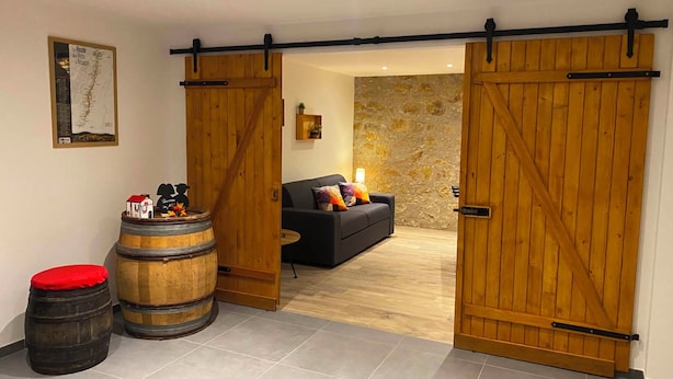 Um quarto com um sofá preto, barris de madeira e uma parede de pedra.