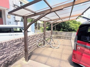 Un área de estacionamiento techada con un aparcamiento para bicicletas, un vehículo rojo y un muro de ladrillo.