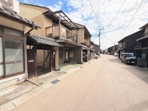 Una calle residencial con casas tradicionales japonesas, cielo despejado y coches estacionados.
