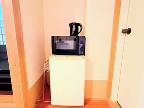 Un refrigerador pequeño blanco con un microondas negro encima, un picaporte y un estante metálico fijado a la pared.