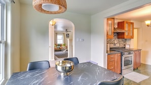 A dining area with a marble table, black chairs, and a silver bowl. There is a kitchen with wooden cabinets and a stove. - 14 Mi to Pittsburgh: Clairton Trailside Retreat (Clairton)