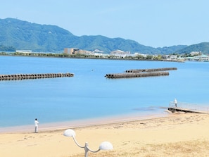 Una spiaggia con una persona che pesca, acqua calma e montagne sullo sfondo.