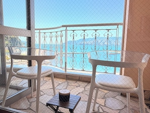 Un balcone con due sedie bianche e un tavolino, vista su un mare cristallino e montagne sullo sfondo.