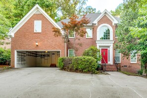 Une maison à deux étages, construite en briques, avec un garage, une porte rouge et un petit porche.