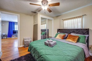 Ein Schlafzimmer mit Bett, Deckenventilator, Kleiderschrank und einem durchgehenden Türrahmen einsehbarer Badezimmer.