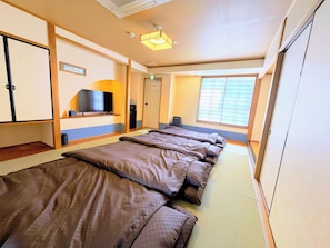 Habitación de hotel con varias camas, televisor, refrigerador pequeño y ventana con persianas.