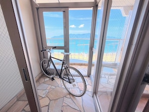 Ein Fahrrad lehnt an einer Glastür, mit Blick auf einen Balkon und einem Steinfußboden.