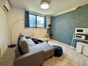 Ein modernes Wohnzimmer mit einer Couch, einem kleinen runden Tisch, einer Stehlampe, einem Topfpflanzen und einer Mikrowelle auf einem weißen Schrank.