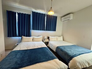 Ein Hotelzimmer mit zwei Betten, einem Nachttisch, einer Lampe und einer Klimaanlage.