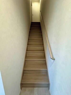 Eine schmale, hölzerne Treppe mit einer Handlauf auf einer Seite, die zu einer Zwischenebene mit einer Lampe führt.
