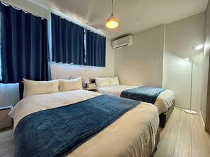 Quarto de hotel com duas camas, uma luminária no teto, ar condicionado e uma mesa de cabeceira com abajur.