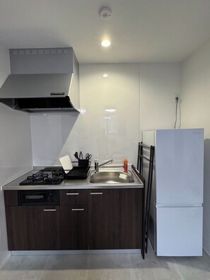 Cozinha compacta com fogão a gás, pia e geladeira branca.