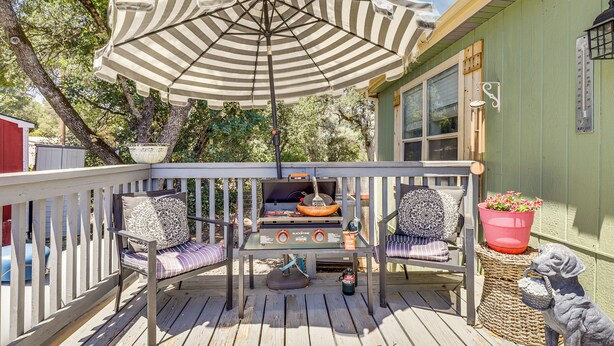 Eine Holzterrasse mit Grill, gestreifter Polsterung und einem großen Sonnenschirm.