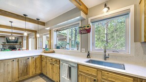 Una cocina con armarios de madera, lavavajillas, pileta y ventana con vista a árboles.