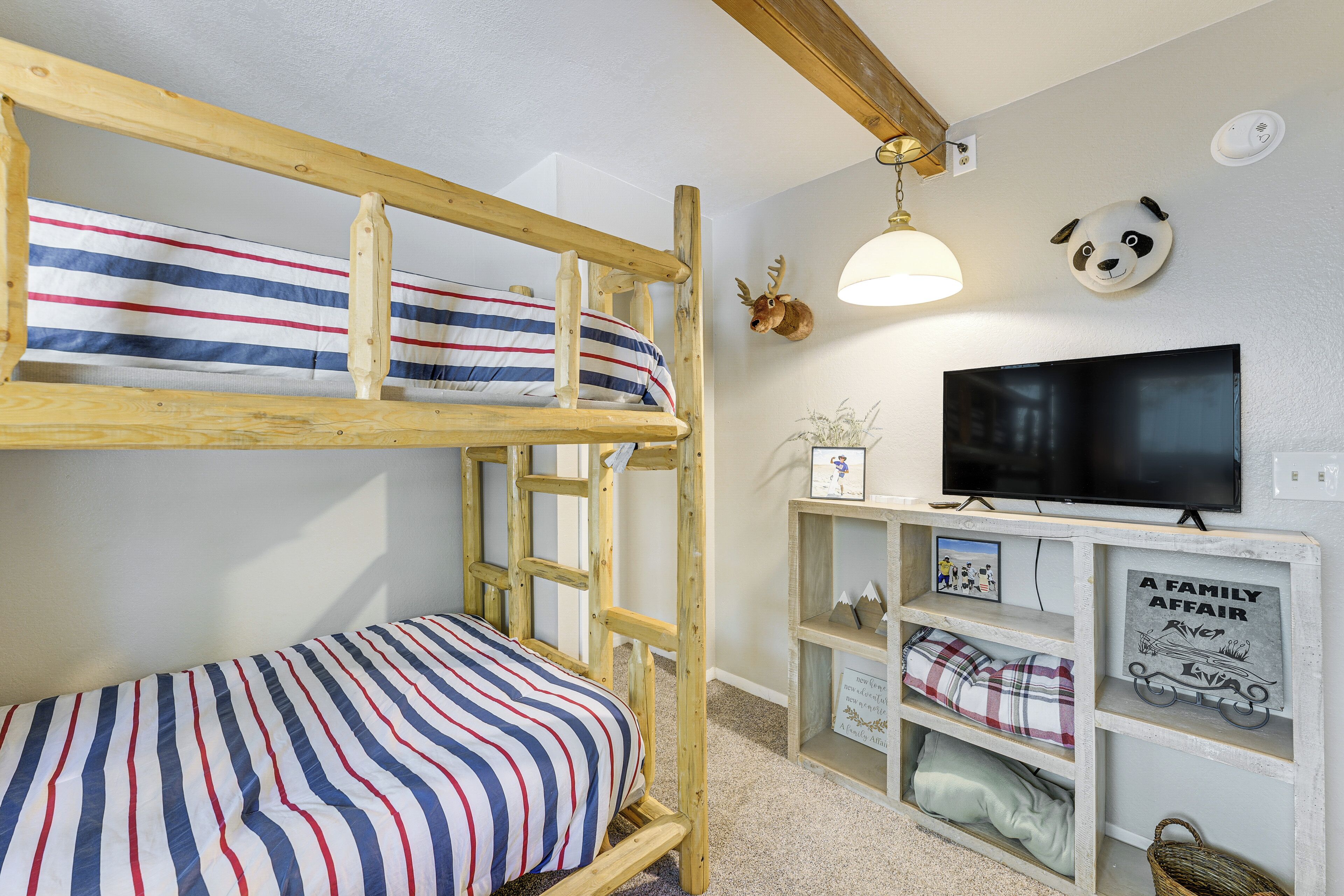 Ein Etagenbett mit gestreifter Bettwäsche, ein aufgehängter Hirschkopf, ein Fernseher und ein Regal mit Familienfotos und einem Schild.