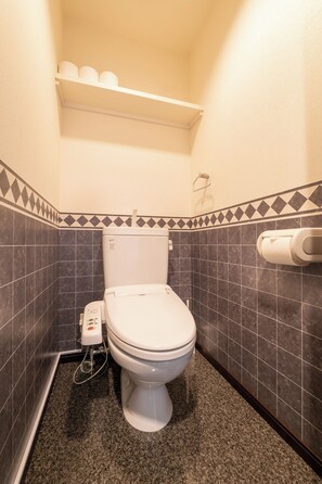 Et lille badeværelse med toilet, håndtørrer og hylde over toilettet.