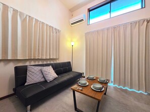 Ein modernes Wohnzimmer mit einem schwarzen Sofa, einem Holztisch mit Schüsseln und Essstäbchen sowie einer Stehlampe.