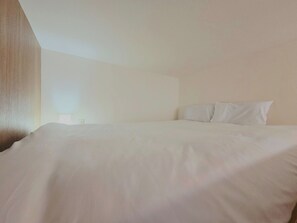 Een eenvoudige, onopvallende hotelkamer met een groot bed, een nachtkastje en een houten accentmuur.