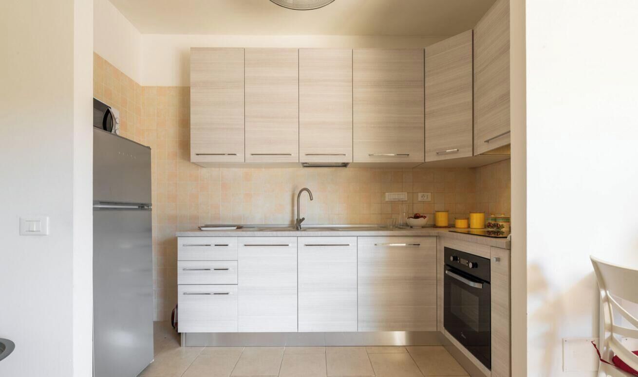 A modern kitchen with light wood cabinets, a stainless steel refrigerator, and a built-in oven.