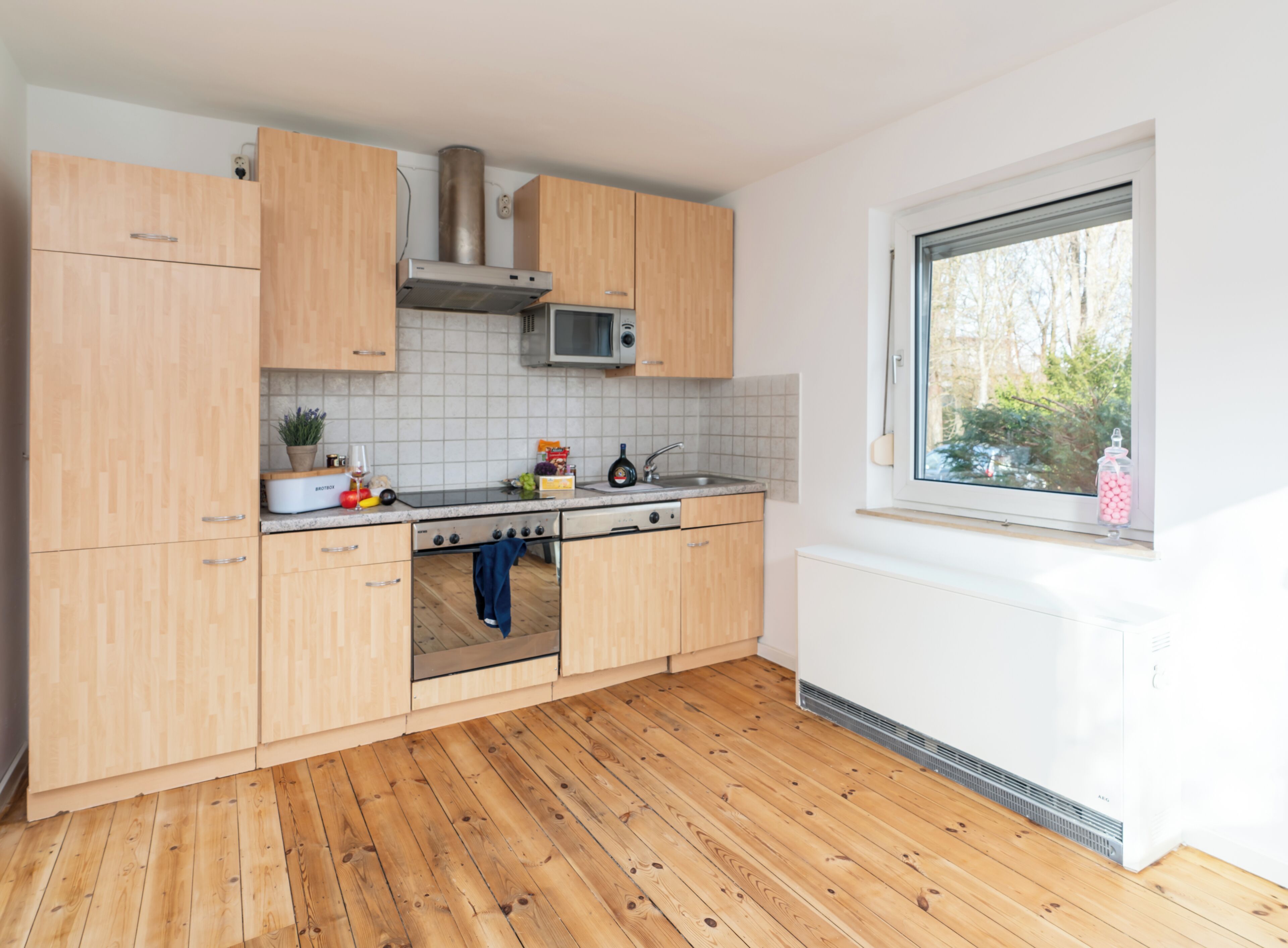 Una cocina moderna con armarios de madera, una campana extractora de acero inoxidable, un microondas y una ventana con vista a árboles.