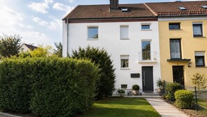 A two-story residential building with a white and yellow facade, a visible balcony, and a well-maintained lawn. - Gemütliches Apartment in Dachau (Freilassing)