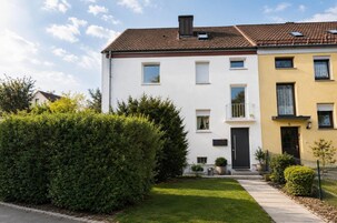 A two-story residential building with a white and yellow facade, a visible balcony, and a well-maintained lawn.