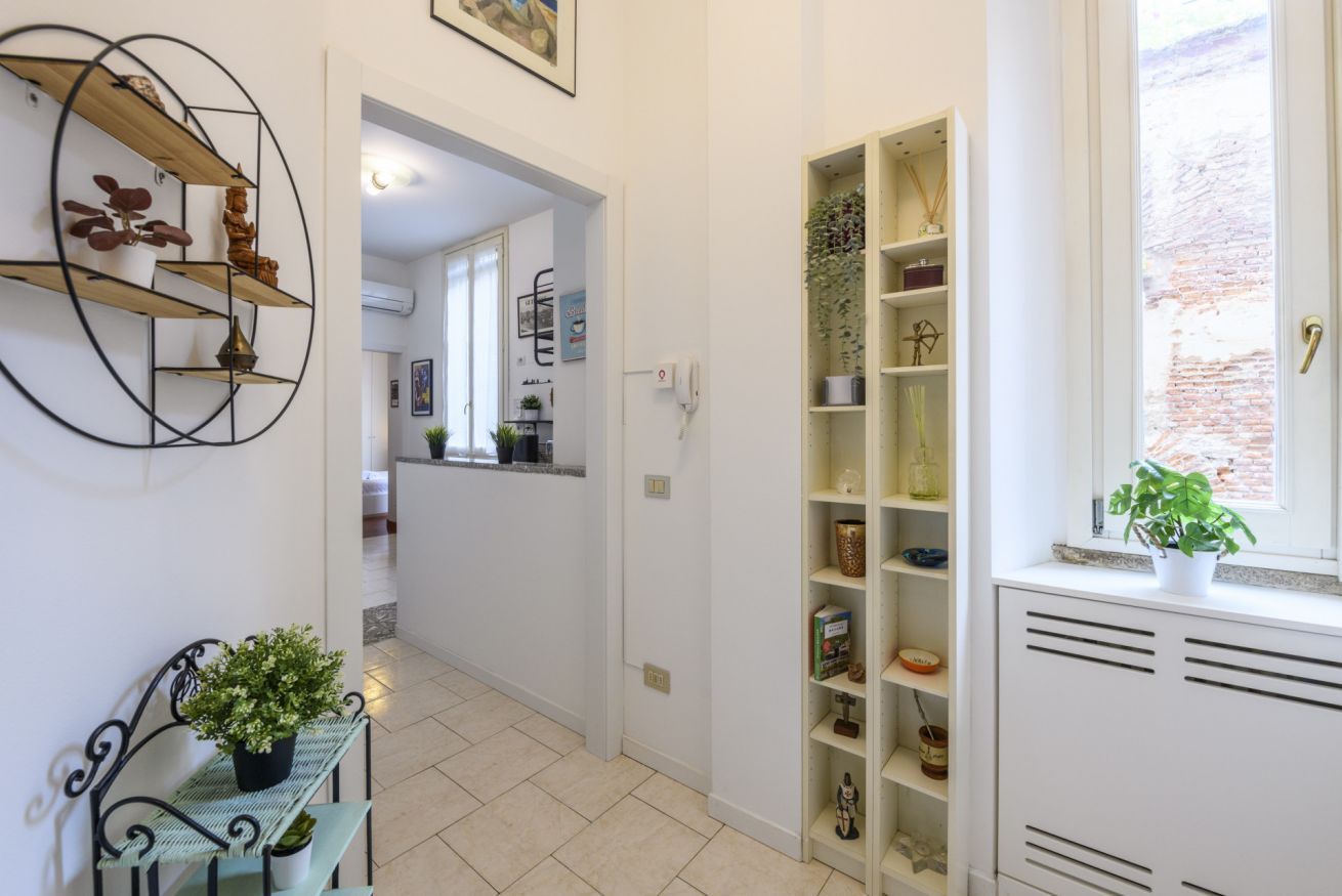 A hallway with a bench, shelves with plants, and a kitchen area in the background.