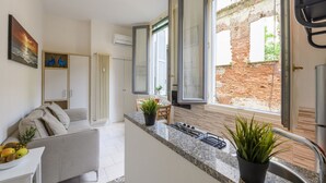 Eine moderne Küche mit einer Granitabdeckung, einem Essbereich mit einem weißen Sofa und Blick auf eine Backsteinmauer durch offene Fenster.