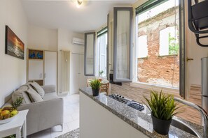 Eine moderne Küche mit einer Granitabdeckung, einem Essbereich mit einem weißen Sofa und Blick auf eine Backsteinmauer durch offene Fenster.