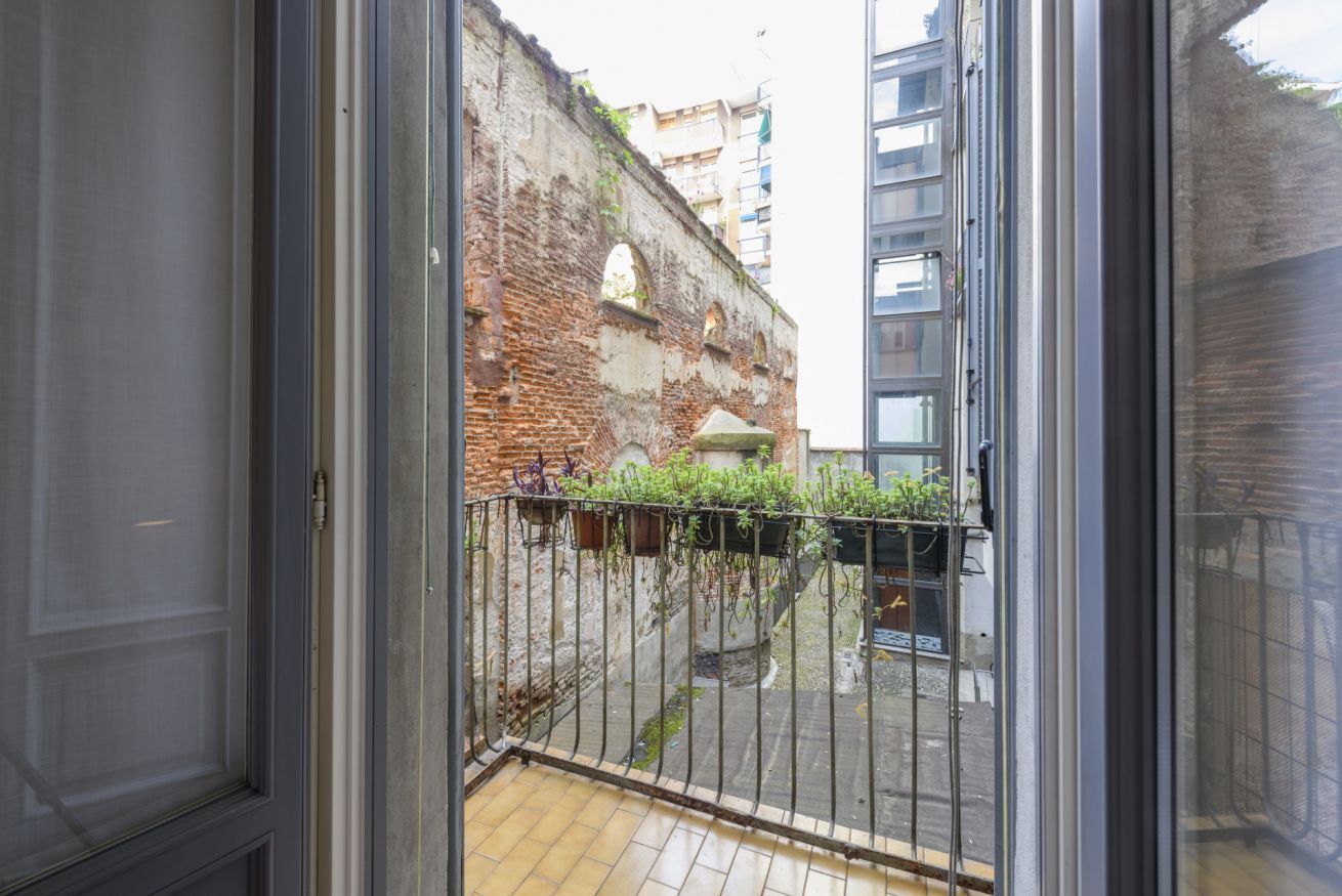 A view through a glass door to a courtyard with a brick wall, a metal fence, and a building in the background.