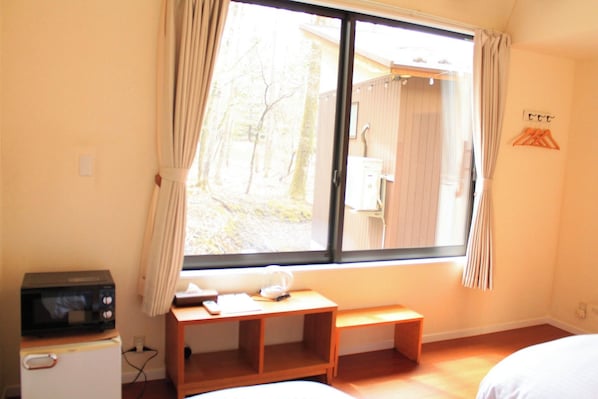 A room with a bed, a small desk, a microwave, and a window with curtains.