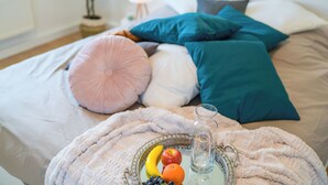 A bed with a variety of pillows, a bedside table with a glass pitcher and a tray of fruit.