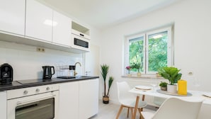 A modern kitchen with white cabinets, a built-in oven, and a dining area with a table and chairs.