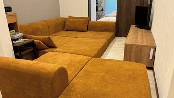 A modern living room with a sectional sofa, a small table with a printer, and a TV on a wooden stand.