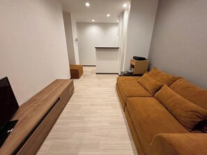 Uma sala de estar moderna com um sofá, TV e uma pequena mesa com um alto-falante.