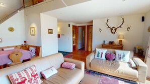 A cozy living room with a sofa, a dining table with checkered tablecloths, a wooden cabinet, and a wall-mounted deer head decoration. - Chesa Iva is situated in one of the most sought-after residential locations in C (Celerina/Schlarigna)