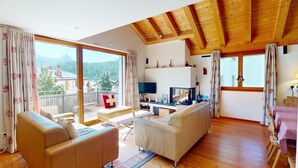 A spacious living room with a balcony, wooden ceiling beams, and a TV. - Chesa Iva is situated in one of the most sought-after residential locations in C (Celerina/Schlarigna)