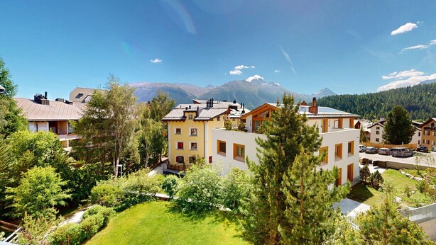 A residential area with houses, a green lawn, and mountains in the background. - Chesa Iva is situated in one of the most sought-after residential locations in C (Celerina/Schlarigna)