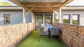 Eine überdachte Terrasse mit Tisch und Stühlen, einer Holzbalkendecke und Blick auf die Umgebung.