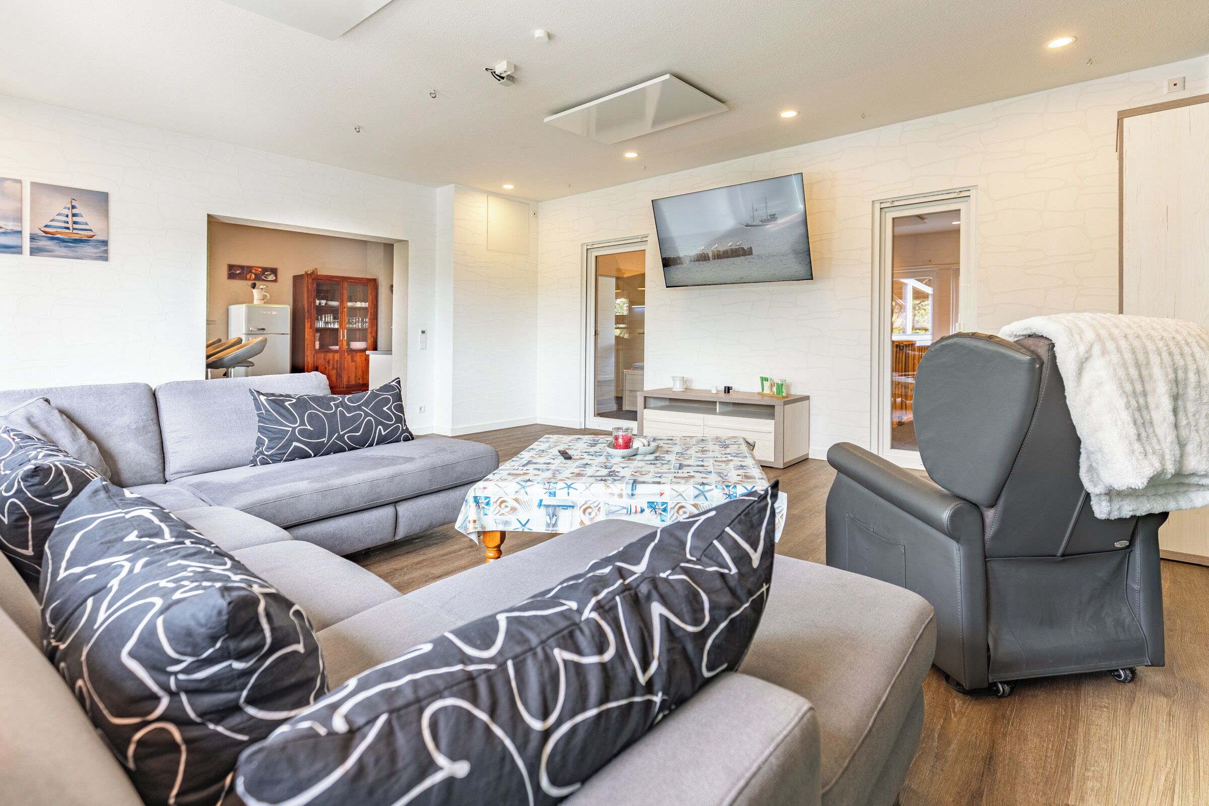 A modern living room with a sectional sofa, a recliner, a flat-screen TV, and a dining area with a table and chairs.