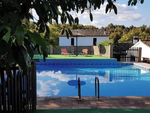 A swimming pool with two lounge chairs, a small building with a tiled roof, and a wooden fence.