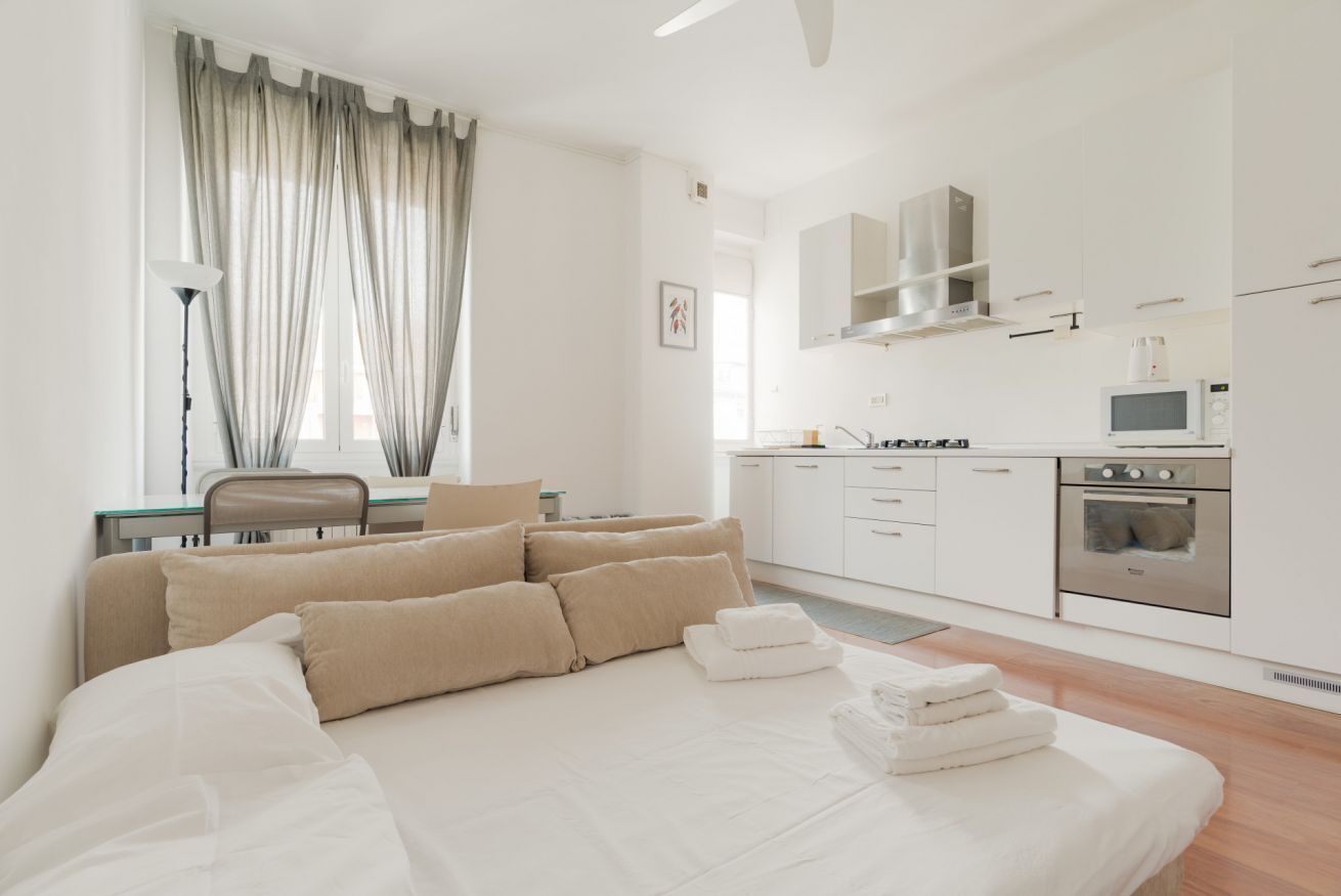 Ein modernes Hotelzimmer mit Bett, Schreibtisch, Stuhl, einer Küchenzeile und einem Fenster mit Vorhängen.