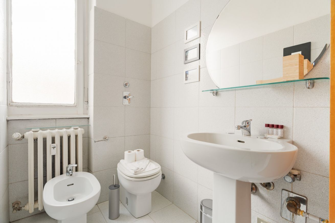 Un baño moderno con bidé, inodoro, lavamanos y repisa de vidrio.